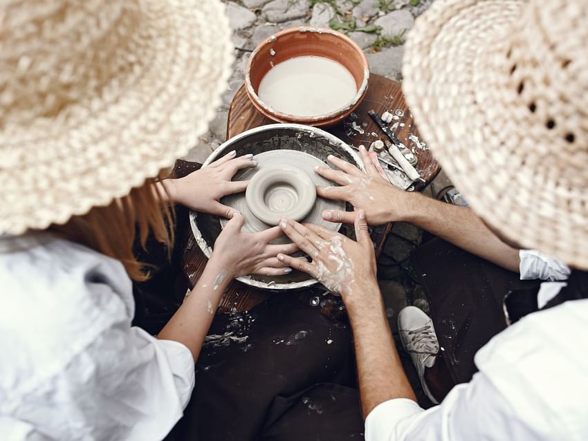 Two people in hats with hands on a pottery wheel, shaping clay, a unique and creative experience at Marquis Los Cabos Resort