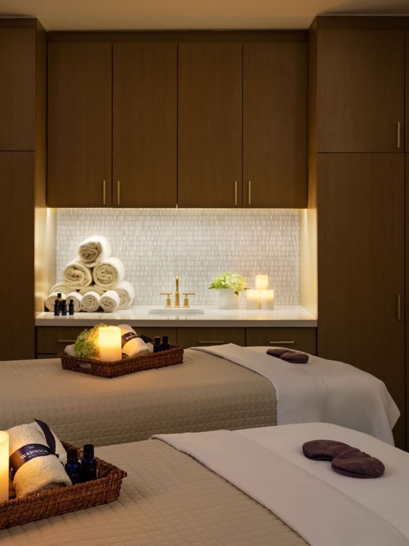 Two massage tables by wooden cabinets under glowing candles in a serene spa at Warwick Melrose Dallas