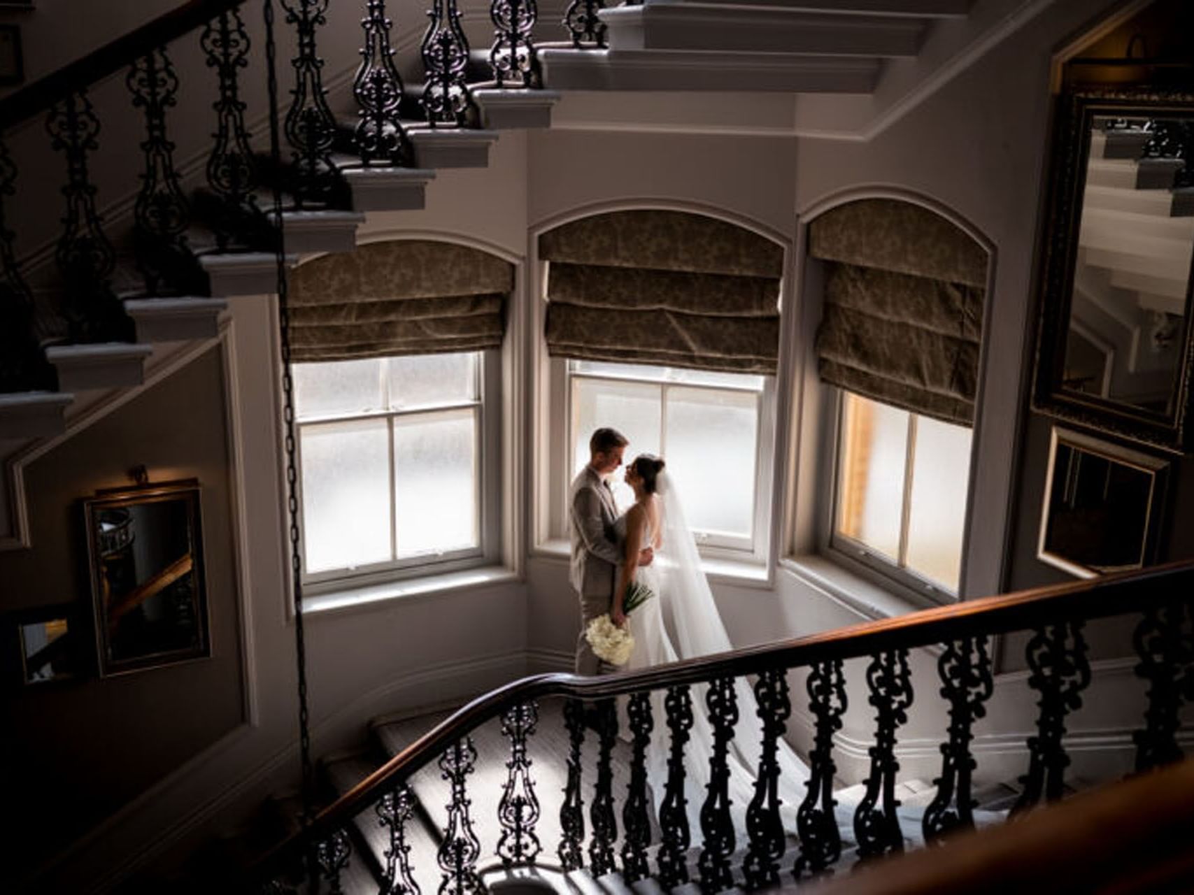 Couple posing in wedding attire embracing on a staircase by windows at The Milner York