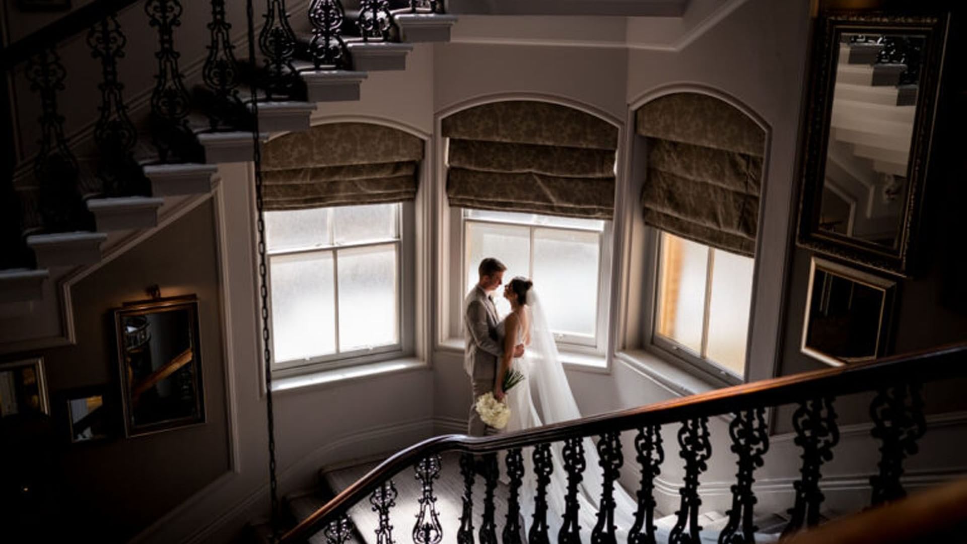 Couple posing in wedding attire embracing on a staircase by windows at The Milner York