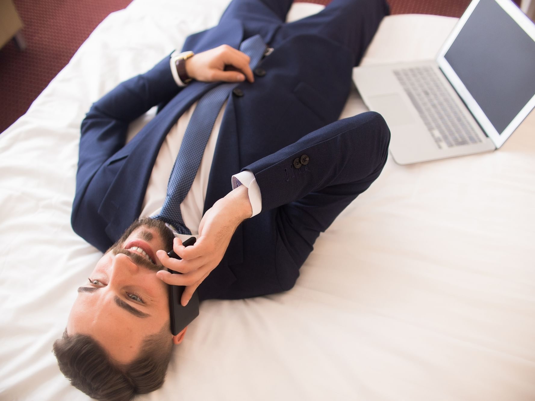 A man in suite lying on bed taking a call at Royal Rose Hotel