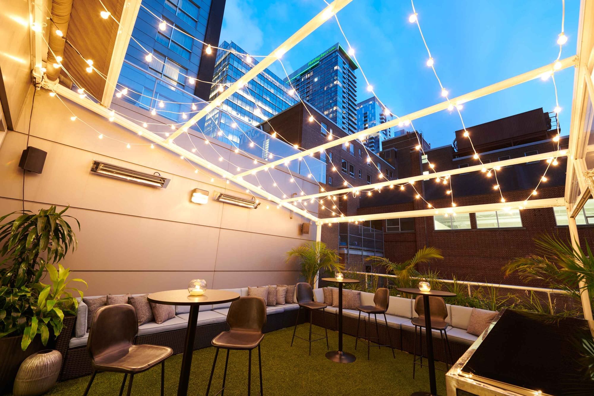 Stylish rooftop patio at Warwick Hotels and Resorts, featuring high tables, a bar, and festive string lights at night
