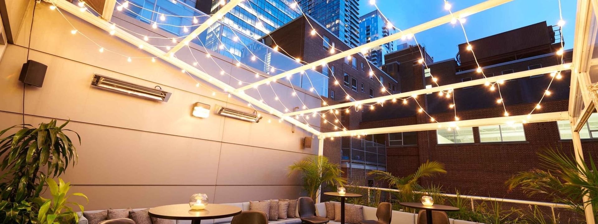 Terrasse élégante sur le toit du Warwick Hotels and Resorts, avec tables hautes, bar et guirlandes lumineuses festives la nuit.