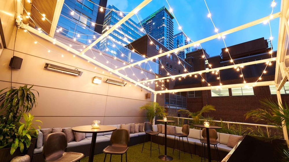 Terrasse élégante sur le toit du Warwick Hotels and Resorts, avec tables hautes, bar et guirlandes lumineuses festives la nuit.