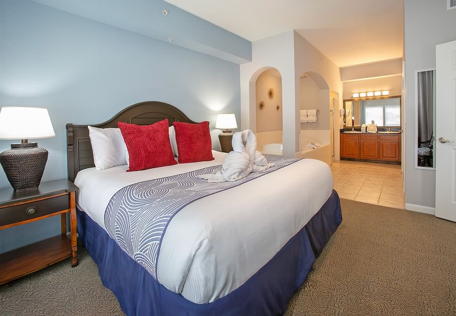 A hotel room with a king-sized bed, a bathroom with an archway, and a tiled floor.