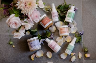Selection of spa bottles and cosmetic jars arranged with fresh flower petals on tile at La Tourelle Hotel and Spa