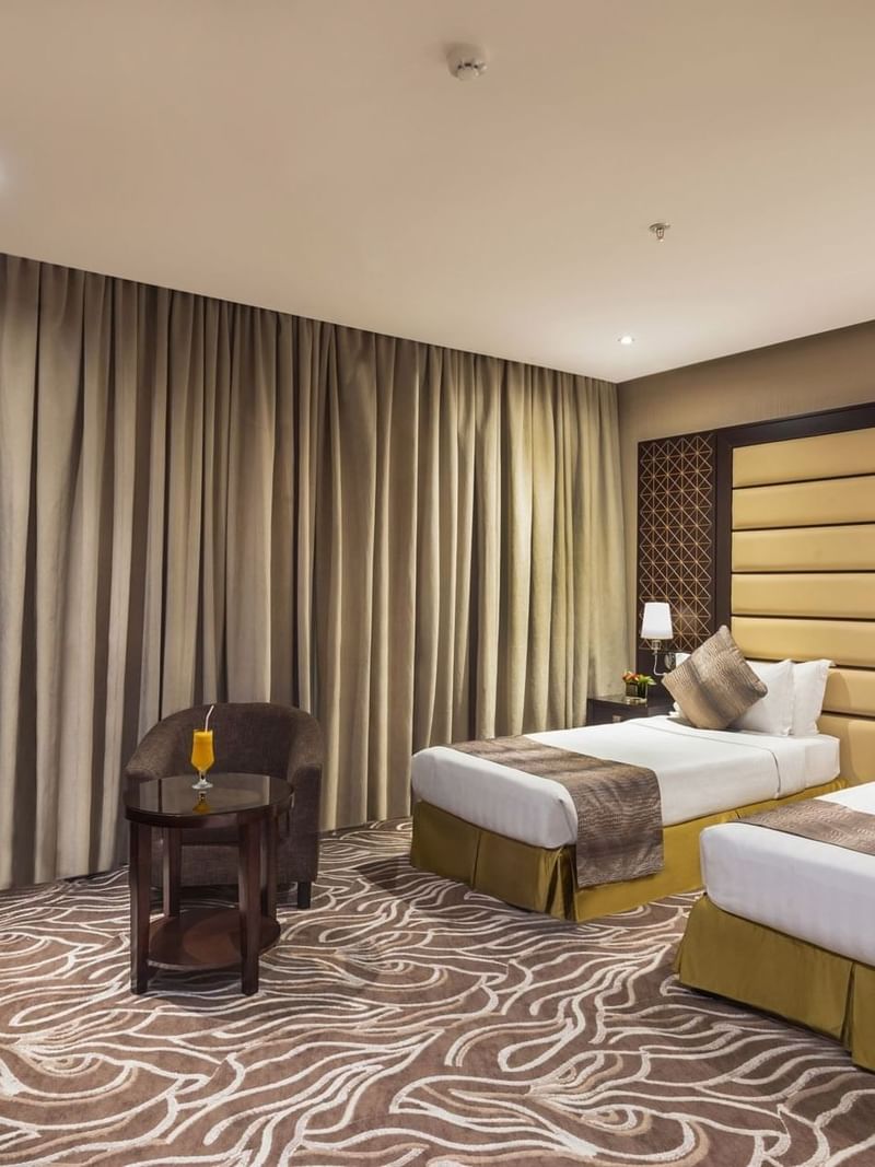 Two beds by a round table with juice under a tan curtain in Deluxe King / Twin Room at Naviti by Warwick Al Khobar