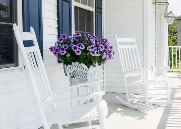 2 white chairs on the front porch next to a white wicker basket filled with purple flowers at Ogunquit Collection