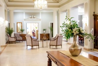Plush armchairs by small tables under a glowing crystal chandelier in a bright lobby area at Rodd Charlottetown Hotel