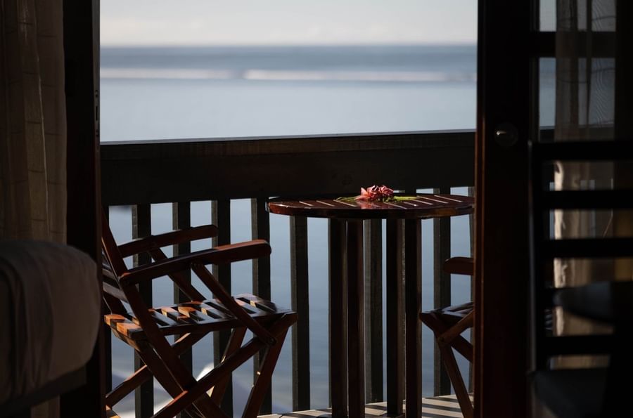 Wooden chairs by a round table under a dark railing in Ocean View Rooms at Warwick Fiji Resort and Spa