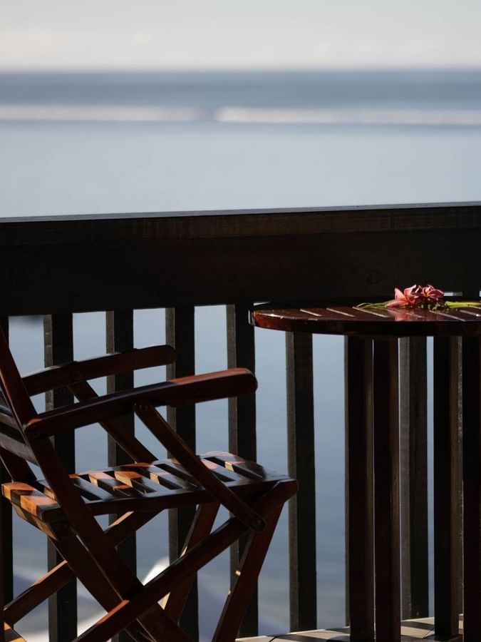 Wooden chairs by a round table under a dark railing in Ocean View Rooms at Warwick Fiji Resort and Spa