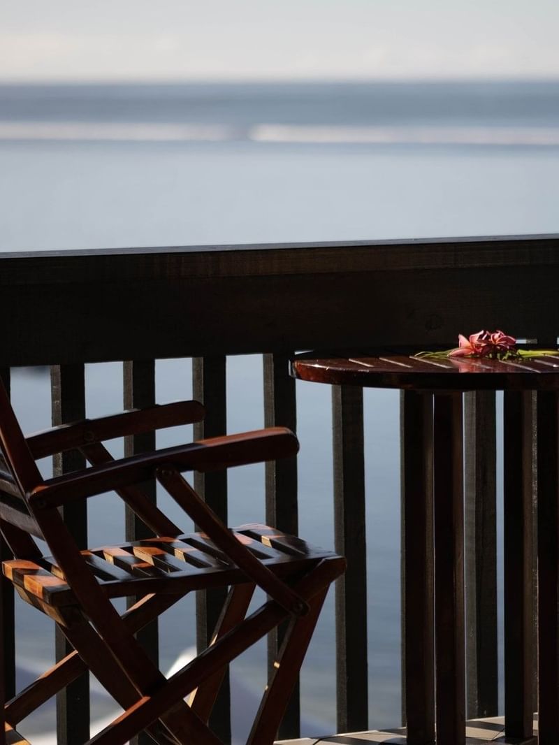 Wooden chairs by a round table under a dark railing in Ocean View Rooms at Warwick Fiji Resort and Spa
