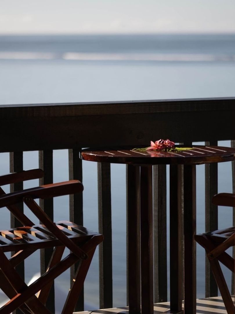 Wooden chairs by a small round table on a balcony overlooking the calm blue ocean at Warwick Hotels & Resorts