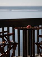 Wooden chairs by a small round table on a balcony overlooking the calm blue ocean at Warwick Hotels & Resorts