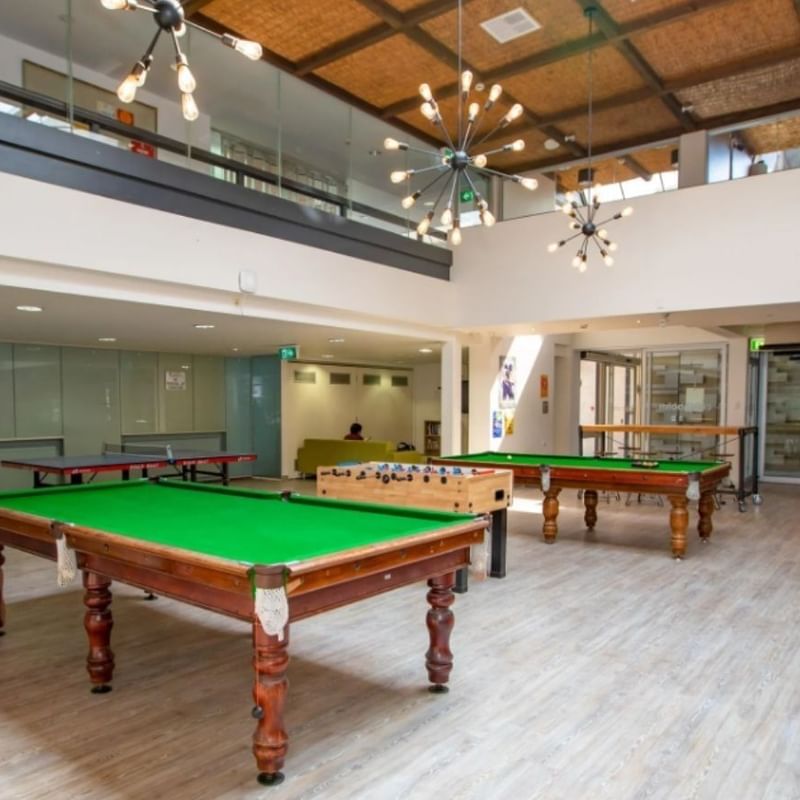 Large billiards room with three green tables and modern decor at La Trobe University - Chisholm College.