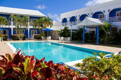Serene pool area is surrounded by colorful plants, and charming white buildings under a clear blue sky at Bay Gardens Inn