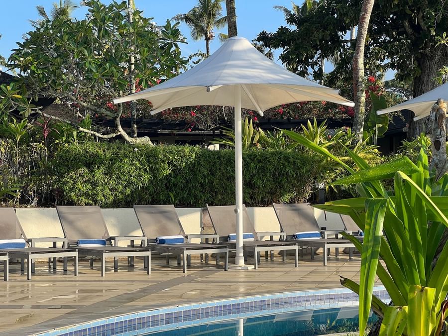 Sun loungers with towels under umbrellas by a pool at Warwick Le Lagon Vanuatu.