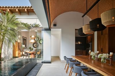 Casa Campanas dining room with a long wooden table and woven pendant lamps by the pool at Singular Signature Residences