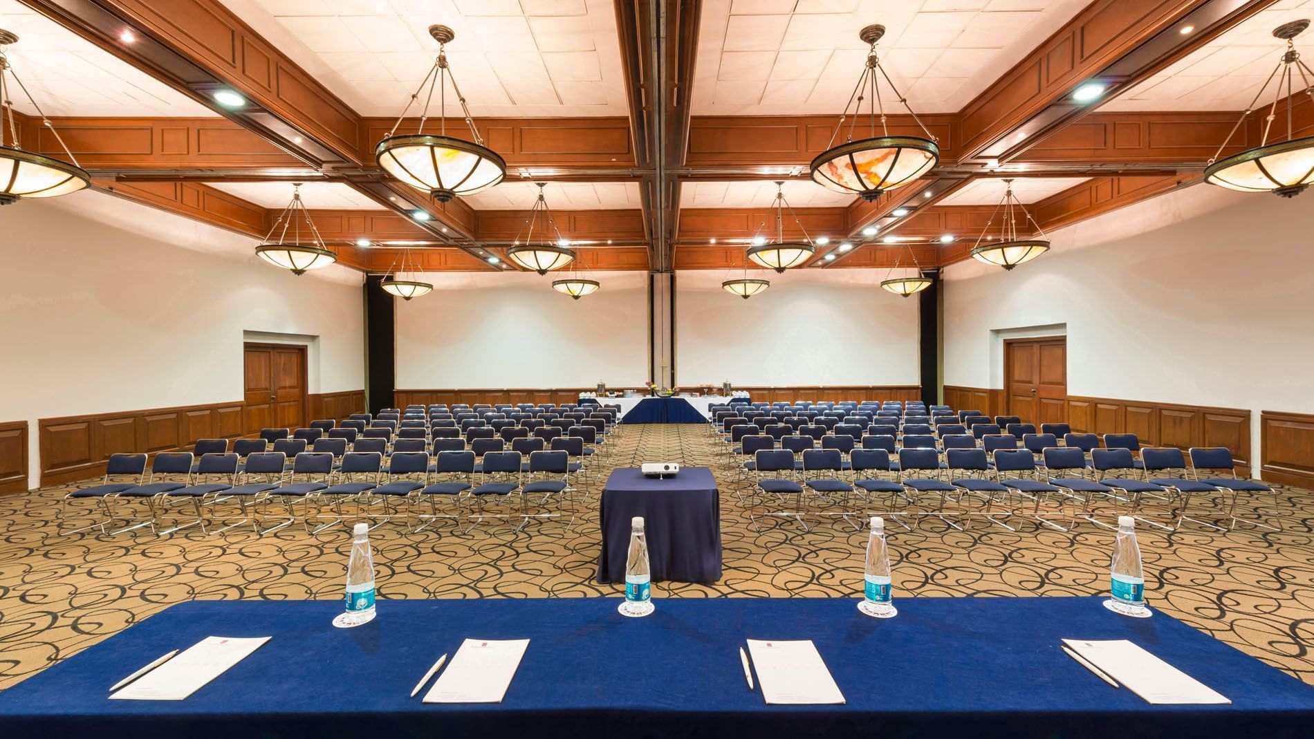Large theater-style Camino Real meeting room featuring rows of blue chairs and chandeliers at Camino Real Puebla Angelopolis