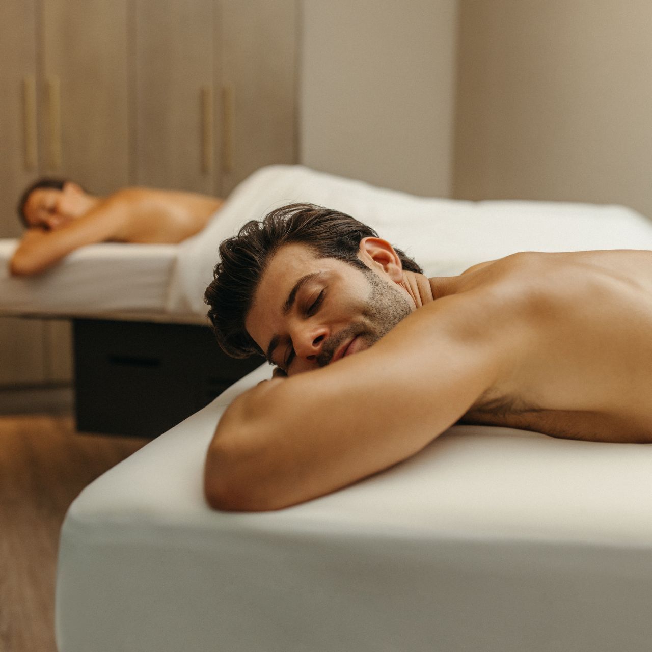 Man lying on a massage table in a spa, with another person in the background.