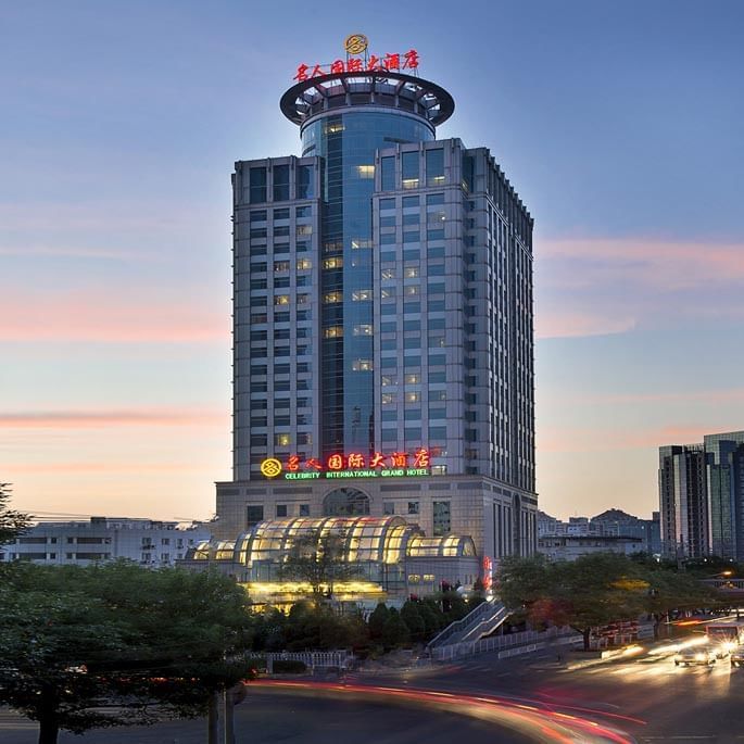 Exterior view of Celebrity International Grand Hotel at sunset with city traffic light trails