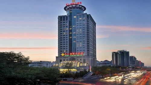 Exterior view of Celebrity International Grand Hotel at sunset with city traffic light trails
