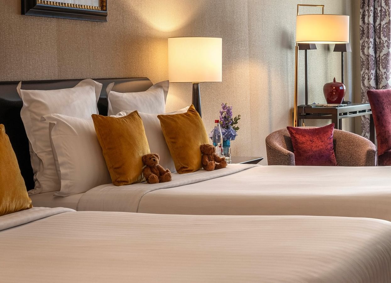 Plush twin beds by a round table with purple chairs in Family room with two queen beds at Warwick Paris Champs Elysées