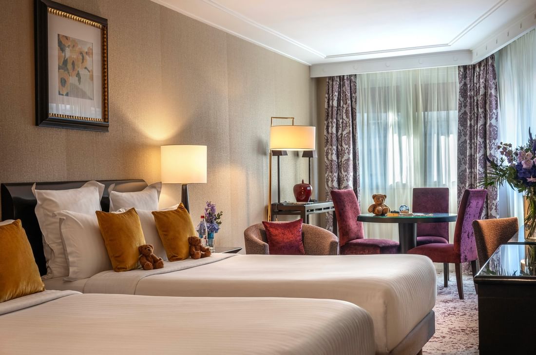 Plush twin beds by a round table with purple chairs in Family room with two queen beds at Warwick Paris Champs Elysées