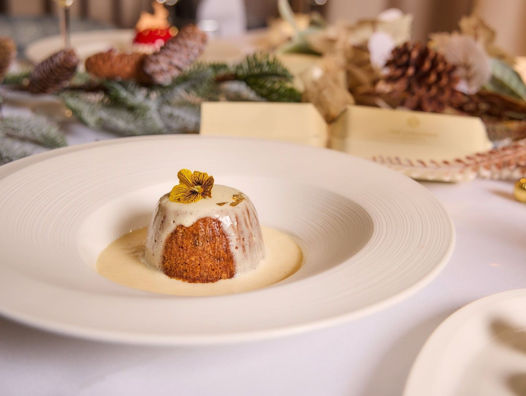 Rich festive pudding drizzled with cream and topped with a yellow flower on a white plate at The Londoner Hotel