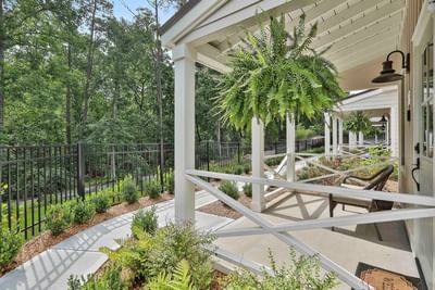 Green fern hangs from a white porch, surrounded by lush greenery and a gravel path by Cottages at Laurel Brooke