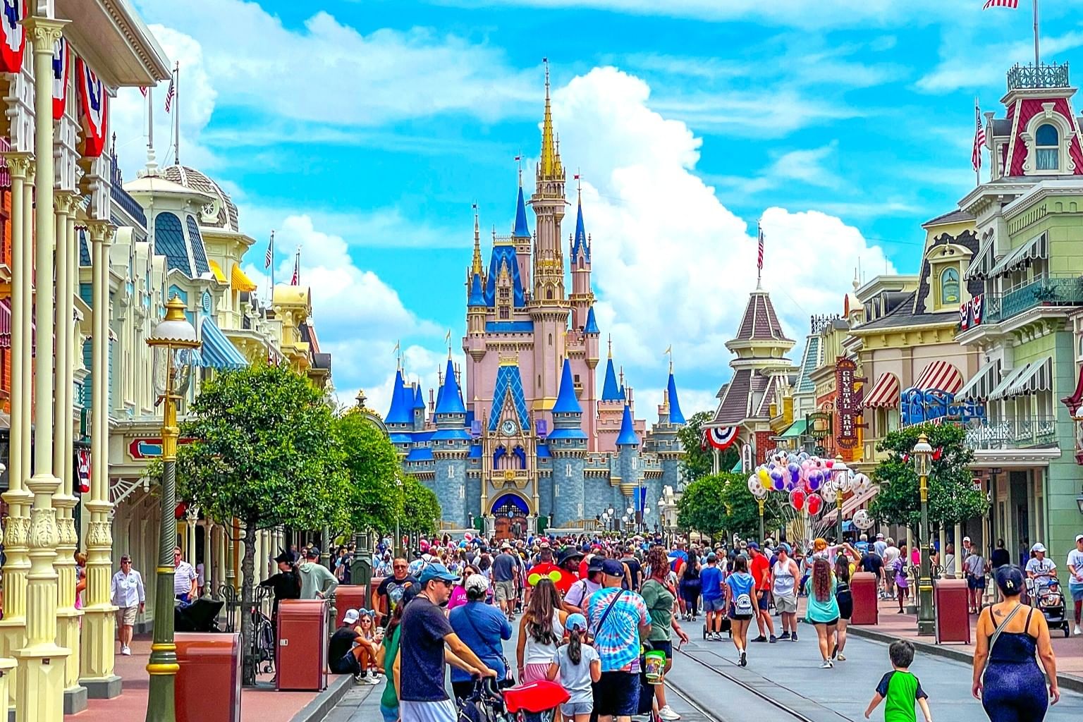 Main Street USA at Walt Disney World with a crowd of people walking toward Cinderella Castle on a sunny day.
