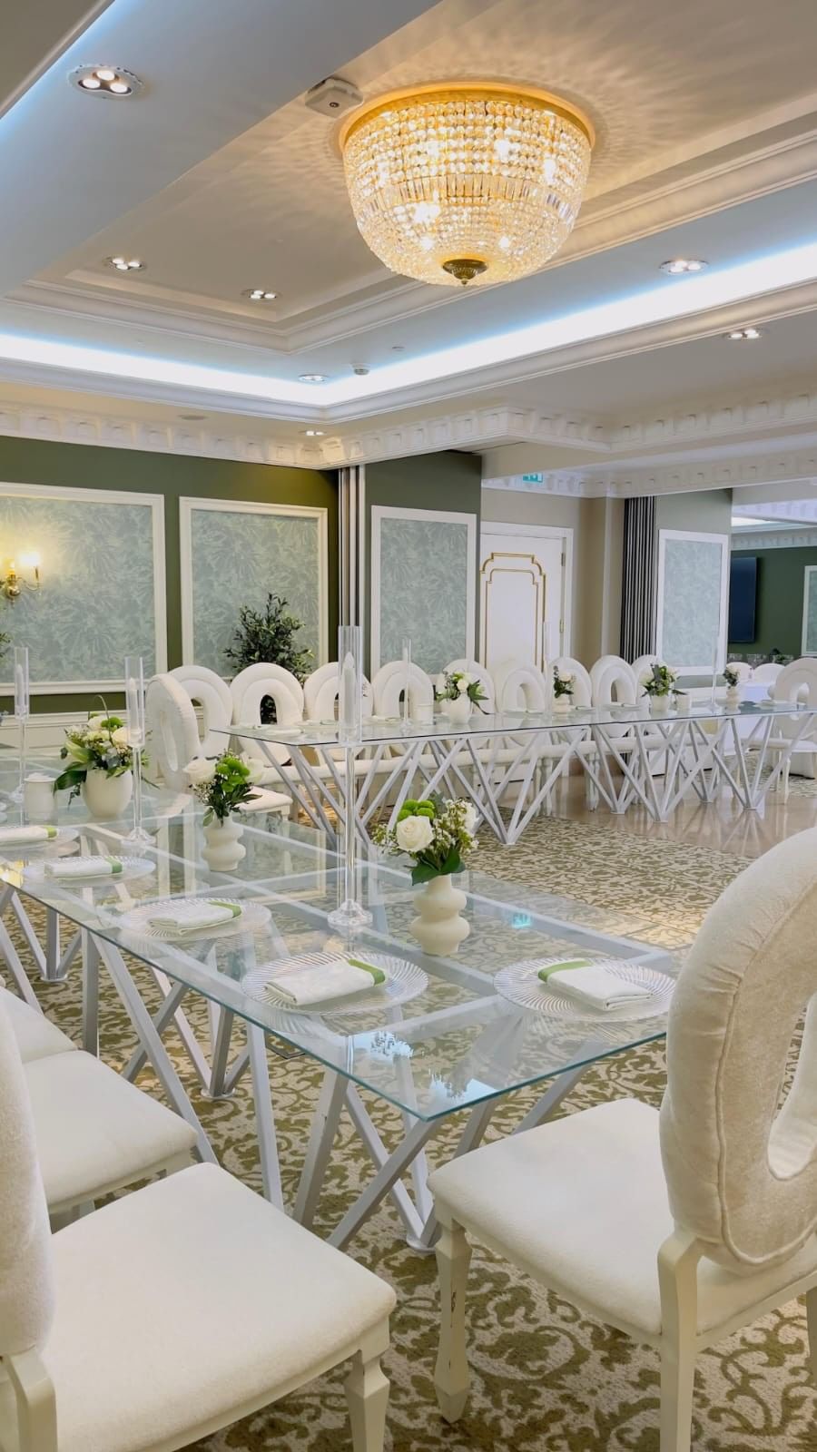 White oval chairs by glass tables under a sparkling crystal dome chandelier in a hall at Warwick Doha Hotel