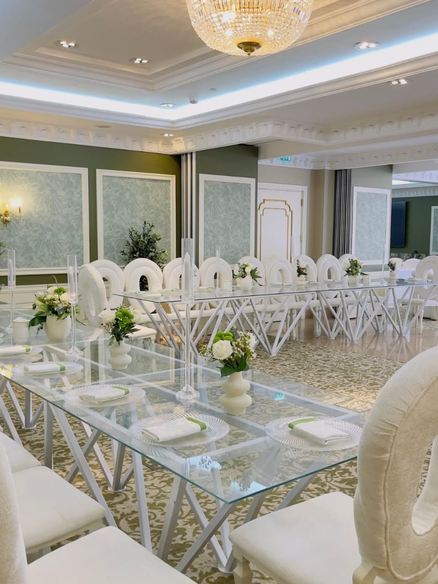 Elegantly set white banquet chairs around a glass table in Gems Ballroom at Warwick Doha.