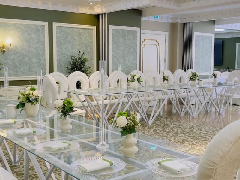 Elegantly set white banquet chairs around a glass table in Gems Ballroom at Warwick Doha.