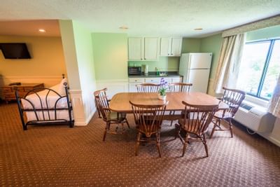 Fox Ridge Resort room with wooden dining table and chairs, kitchen area with fridge, and a bed by the window.