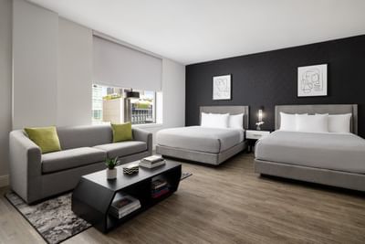 Gray sofa and two beds with art pieces on walls in a modern hotel room at ArtHouse New York City