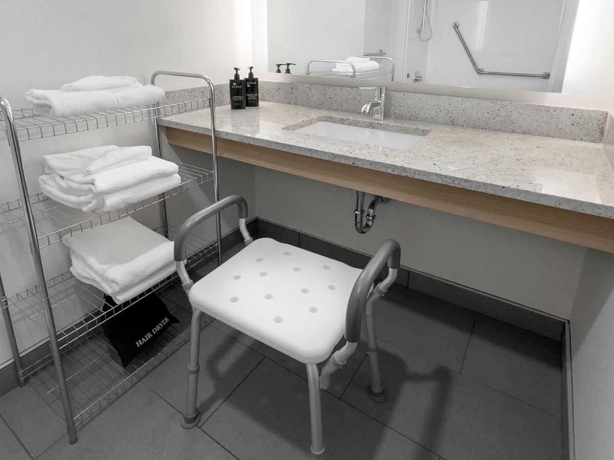 Accessible bathroom with a sink, support chair, towels, and a mirror above the sink.