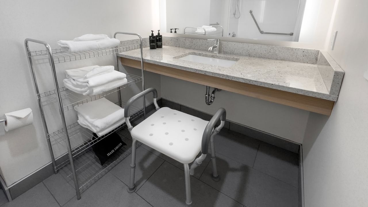 Accessible bathroom with a sink, support chair, towels, and a mirror above the sink.