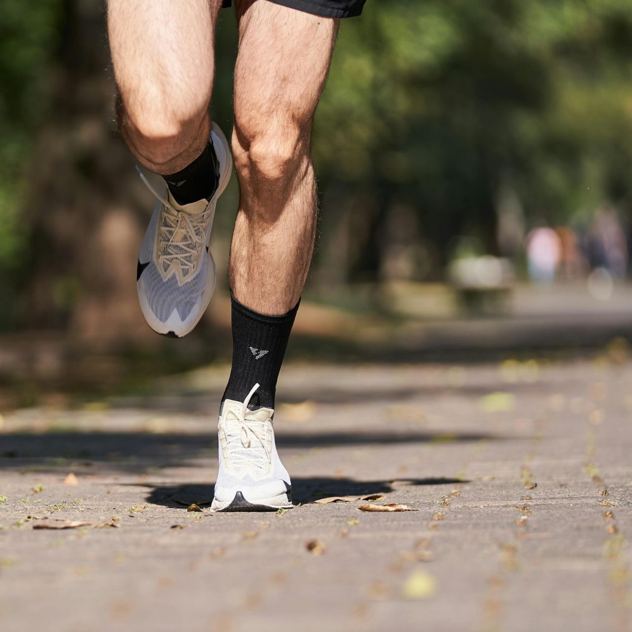 Close-up of runner's legs mid-stride on an outdoor path wearing athletic shoes and black socks 