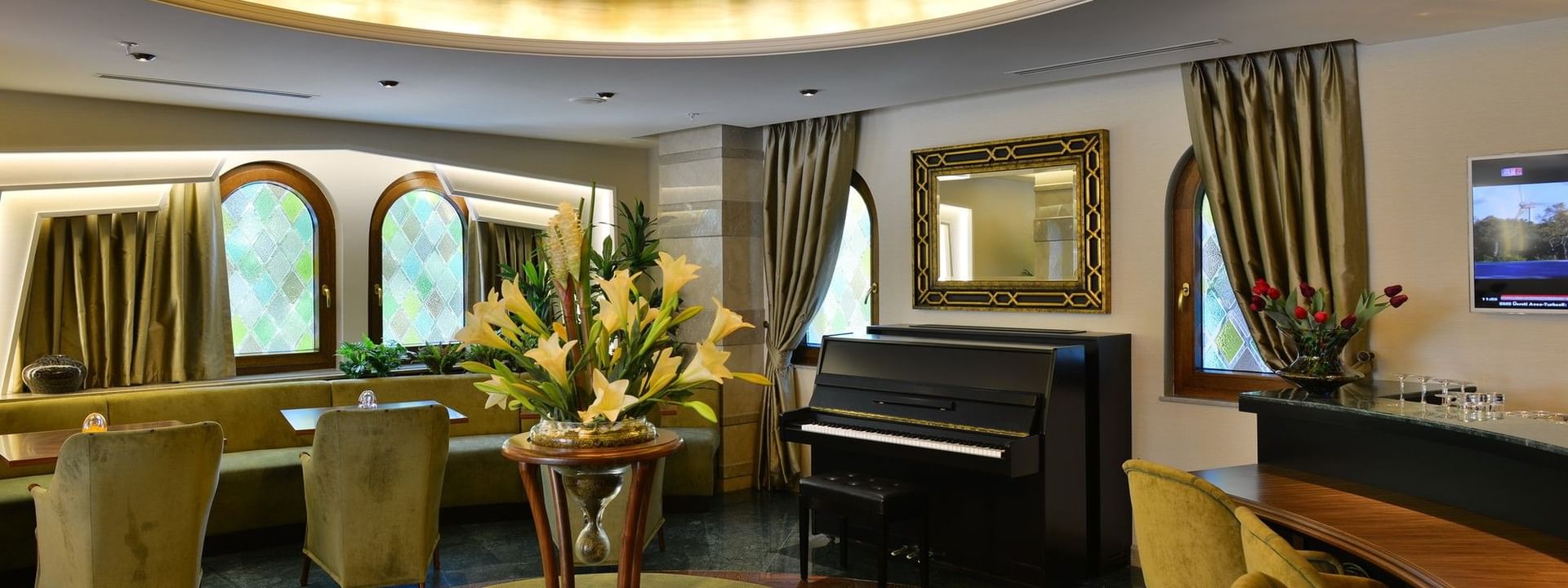 Lobby Lounge with a black piano by a gold-framed mirror surrounding lilies on a table at Warwick Ankara