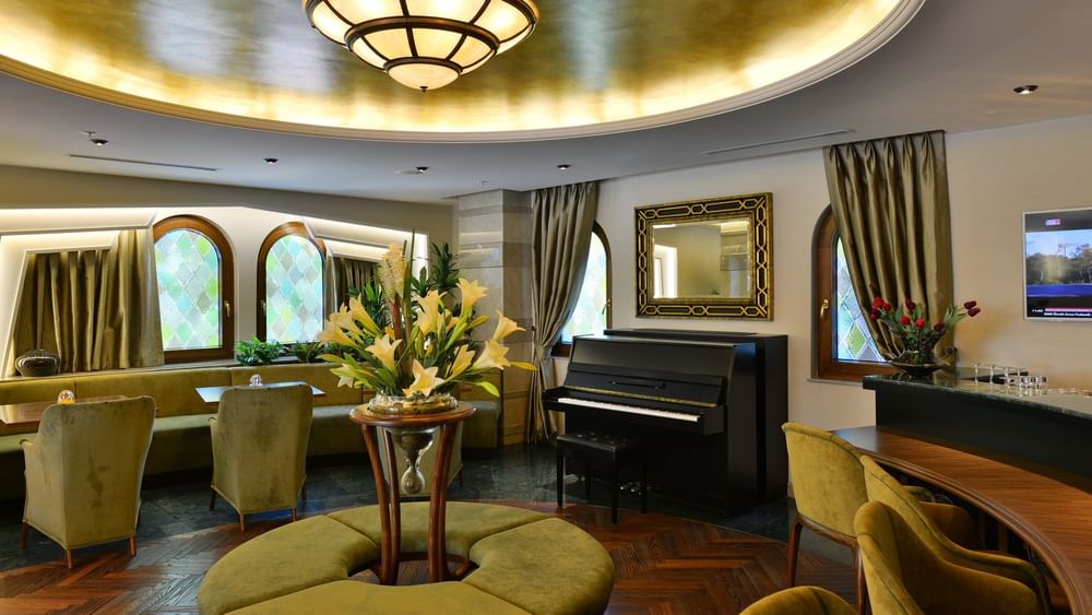 Lobby Lounge with a black piano by a gold-framed mirror surrounding lilies on a table at Warwick Ankara