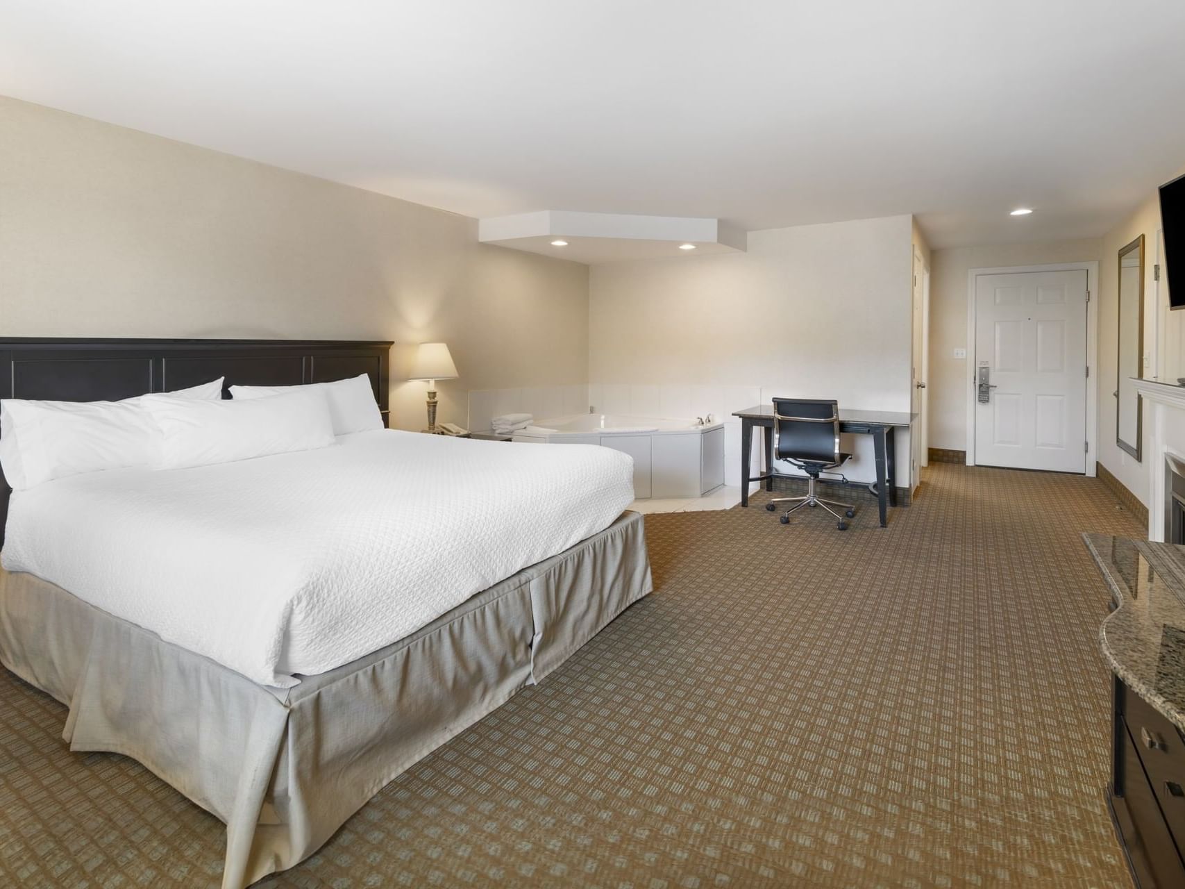 Wall-mounted TV, work desk, and Jacuzzi tub by the comfy bed in Luxury Suites at Ogunquit Hotel & Suites