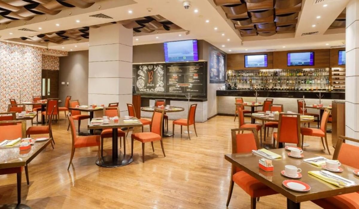 Área de comedor de restaurante con sillas naranjas y mesas preparadas en Camino Real Hotels