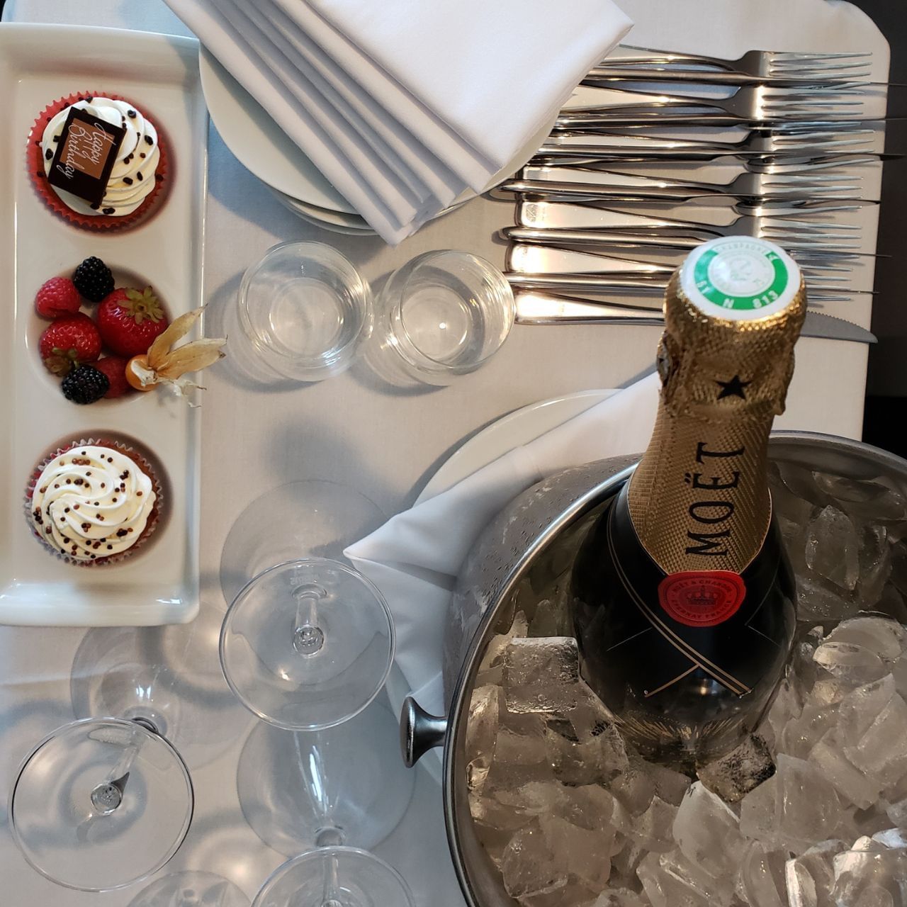 Bottle of champagne in an ice bucket with three cupcakes and strawberries on a platter.