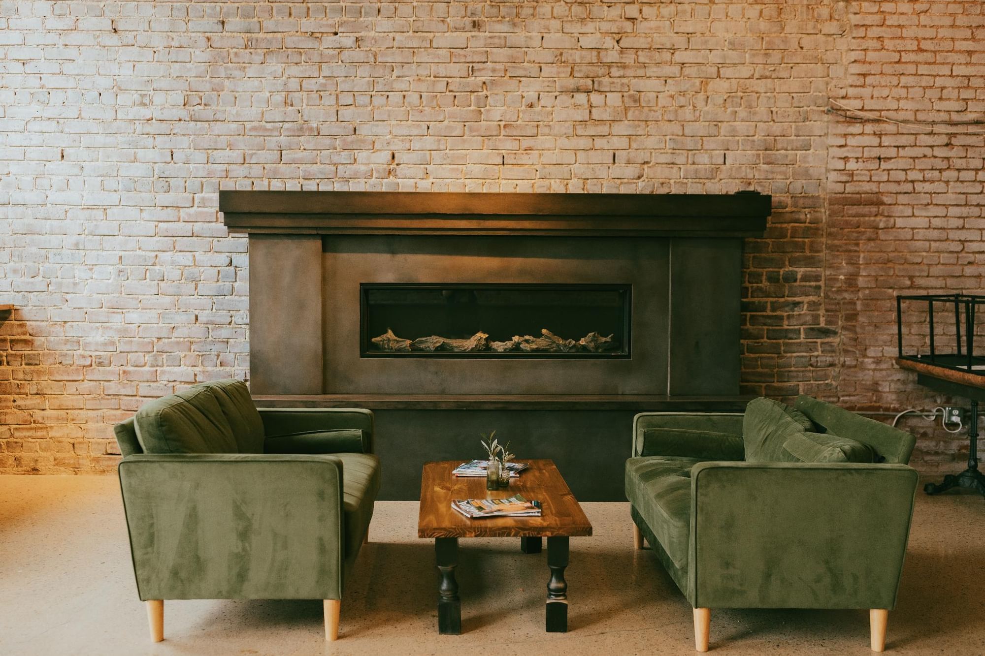 A cozy seating area with two green armchairs and a wooden coffee table in front of a large fireplace.