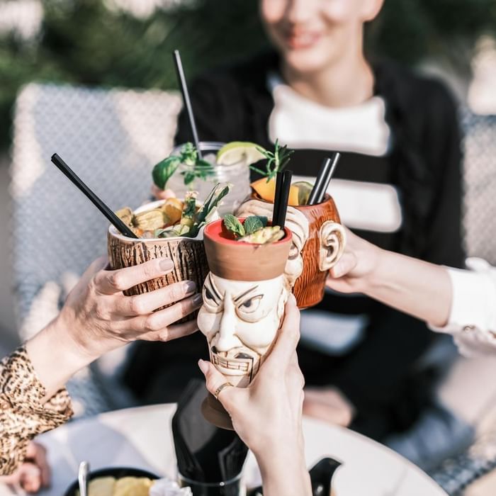 Hands holding tropical drinks garnished with fruit and mint leaves at Falkensteiner Hotel & Spa Jesolo