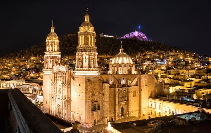 Lit towers by a domed church under a dark sky near the hillside at the Camino Real Pedregal Mexico