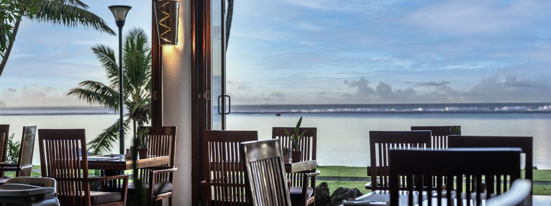 Wooden chairs by a table under a wall light near a large open window in Bula Brasserie at Warwick Fiji Resort and Spa