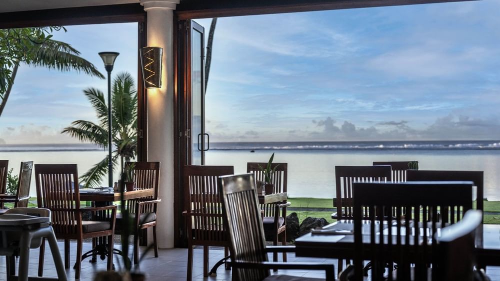 Wooden chairs by a table under a wall light near a large open window in Bula Brasserie at Warwick Fiji Resort and Spa