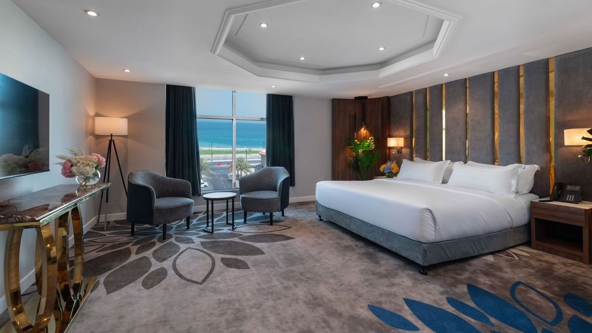 Royal Suite Sea View features King Bed & two grey armchairs by a window at Warwick Al Jubail